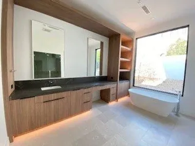Modern bathroom featuring a large mirror, wooden cabinetry, and a soaking tub by a window.