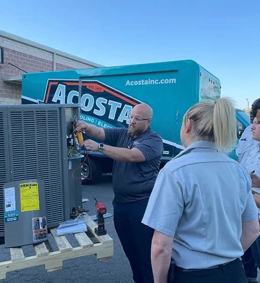 Technician performing electrical maintenance on HVAC unit, with Acosta Heating, Cooling & Electrical service vehicle in background, illustrating professional training and service expertise.