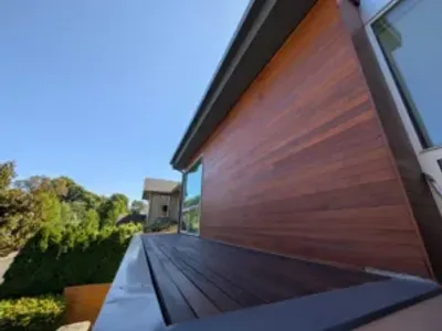 Modern house exterior featuring rich brown wood siding and a matching deck under a clear blue sky.