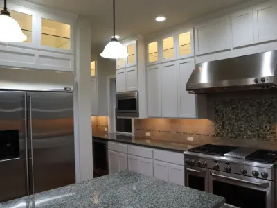 Upscale kitchen featuring elegant white painted cabinets, stainless steel appliances, and under cabinet lighting.