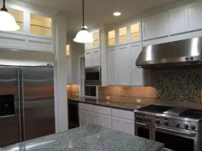 Upscale kitchen featuring elegant white painted cabinets, stainless steel appliances, and under cabinet lighting.