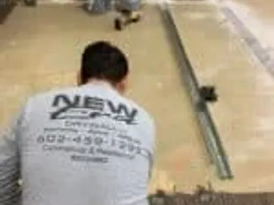 Phoenix Licensed and Bonded Drywall Installer wearing a New Era Drywall Company shirt prepares a floor for metal framing installation
