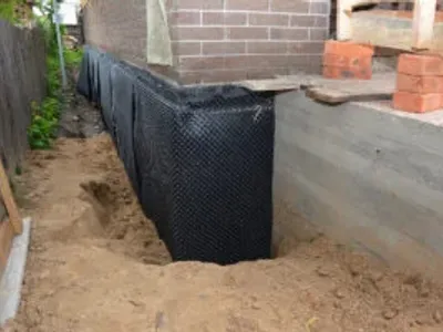 Waterproofing contractor installing dimple mat and drain in a basement corner with rigid foam board insulation.