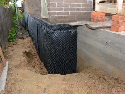 Waterproofing contractor installing dimple mat and drain in a basement corner with rigid foam board insulation.