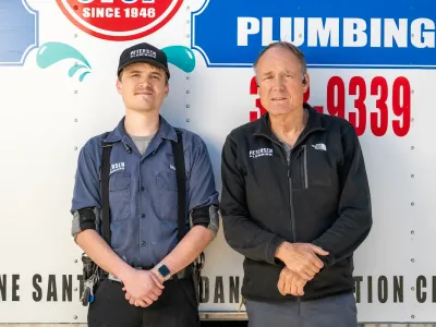 Two generations of Petersens standing in front of plumbing equipment.