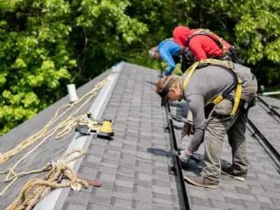 Three Golden Group workers with proper safety equipment installing the foundation for new solar panels on a slanted rooftop.
